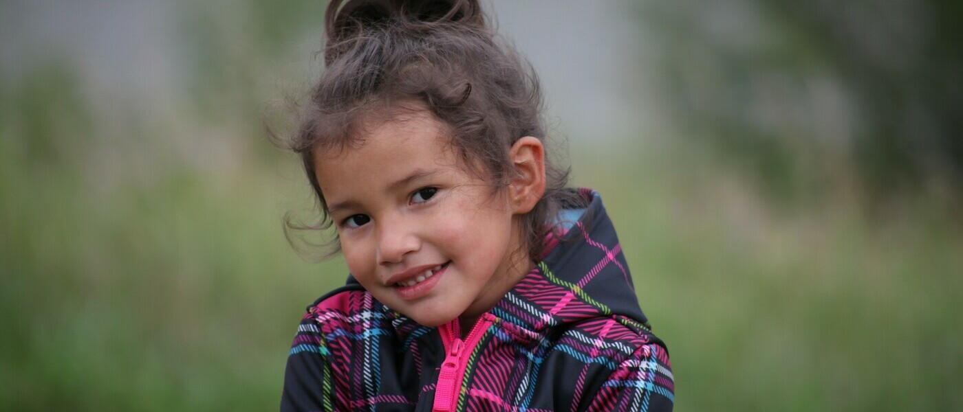 A young girl in a plaid jacket smiles at the camera