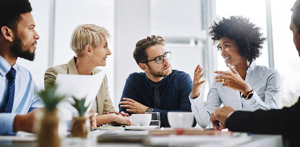 A group of professionals sit at a table with papers and plants