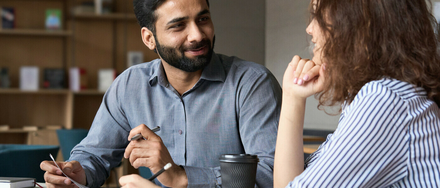 A man smiles at a woman as they discuss work notes in the office