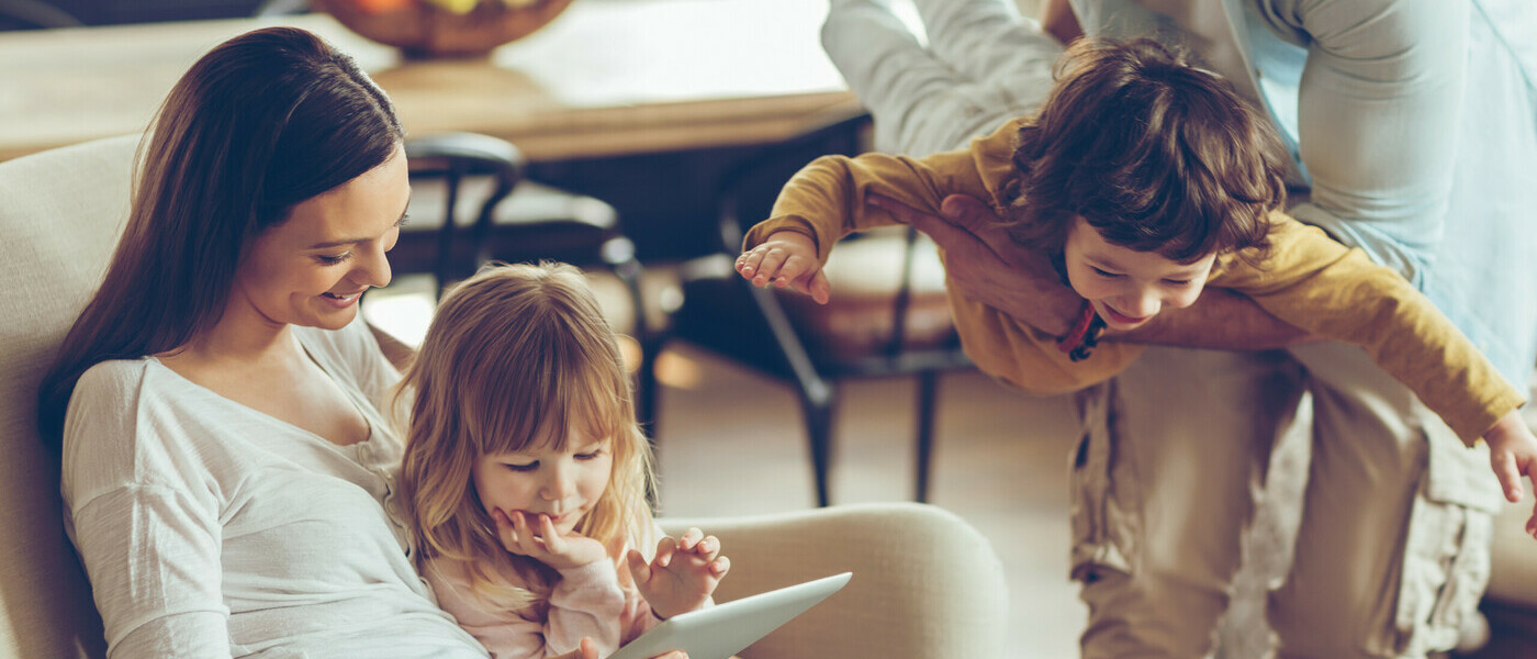 A woman and her daughter reading a blog from a tablet and a man and son playing 